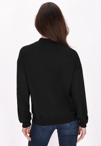 Zwarte sweatshirt met een textured, geometrisch patroon. Heeft een ronde hals en elastische manchetten. Gecombineerd met blauwe jeans.