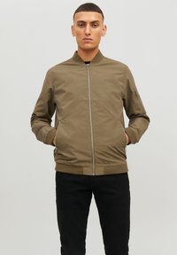 Olive green bomber jacket with a zip front, side pockets, ribbed cuffs, and a smooth matte texture. Features a zipped sleeve pocket.