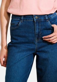 Jeans in denim blu a vita alta con una leggera elasticità, dotati di tasche frontali, cuciture visibili e chiusura con bottone in metallo.