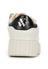Sneaker bianco con suola testurizzata e rialzata. Il retro presenta un accento nera lucida con logo. Parte superiore in pelle liscia e rivestimento interno beige.
