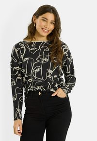 Haut noir à manches longues avec un motif d'art linéaire abstrait en crème. Confectionné dans un tissu doux, il présente un col bateau et une coupe décontractée. Associé à un jean noir.