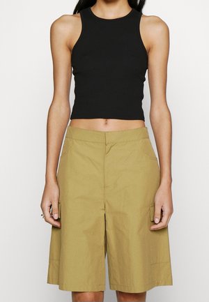Černý krátký top bez rukávů kombinovaný s béžovými kraťasy po kolena s bočními kapsami a volným střihem. Hladká tkanina s mírným leskem.