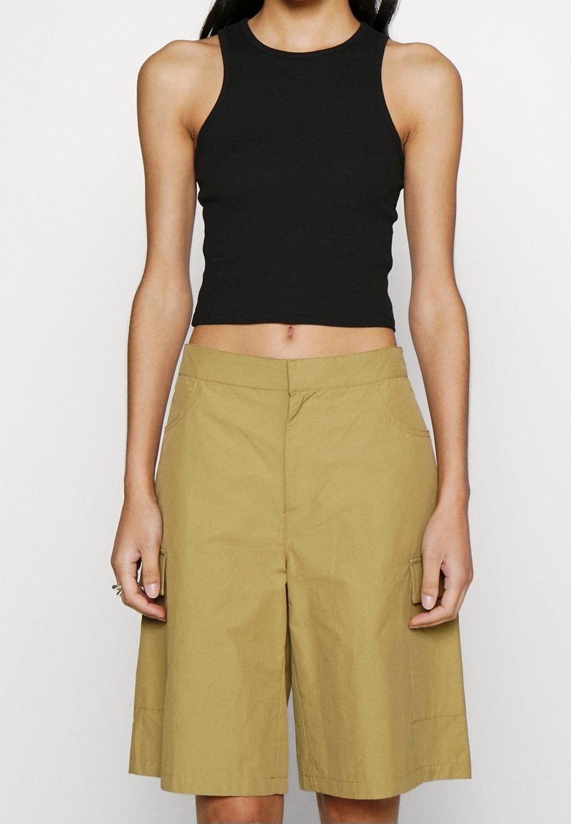 Haut court noir sans manches associé à un short beige jusqu'aux genoux avec poches latérales et coupe décontractée. Tissu lisse avec un léger éclat.