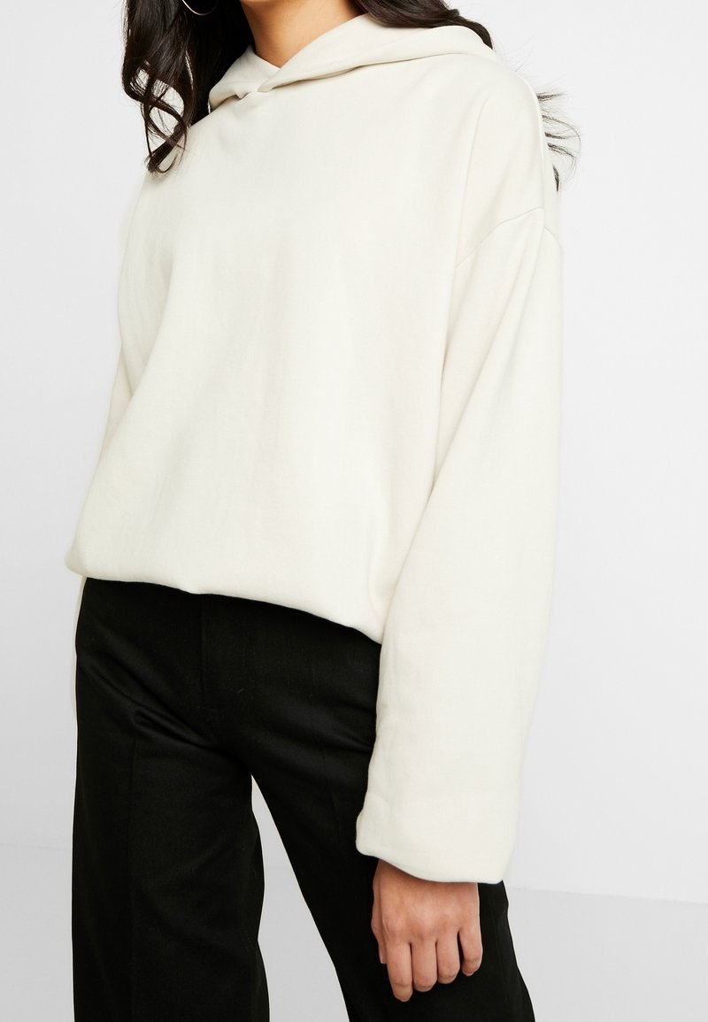 Felpa con cappuccio color crema dalla vestibilità comoda, con maniche lunghe e cappuccio regolabile con coulisse, abbinata a pantaloni neri slim fit. Tessuto dalla texture morbida.