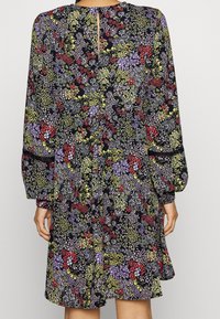 Šaty s květinovým potiskem v tmavě námořnické barvě s červenými, zelenými a fialovými květy. Dlouhé rukávy s elastickými manžetami, otevřený klíčový otvor na zádech a zúžený pas.