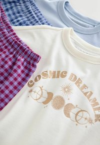 Trzy ubrania: kremowy sweatshirt z złotym napisem "COSMIC DREAMER" i grafiką o tematyce niebiańskiej, jasnoniebieska koszula oraz fioletowo-szachownicowe spodenki.