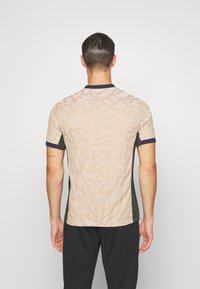 Tílko s krátkým rukávem sportovního stylu s béžovým texturovaným vzorem, tmavě zelenými bočními panely a námořnickým límcem. Jednoduchý design pro aktivní nošení.