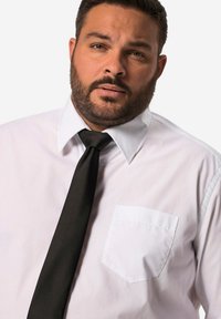 Camicia bianca con cravatta nera, dotata di una tasca sul petto e colletto a punta, realizzata in un tessuto liscio e dalla trama uniforme.
