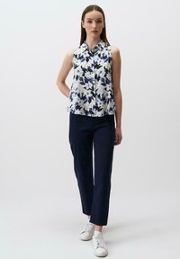 Bezrękawnik w kwiaty w niebiesko-białym wzorze, z zapięciem na guziki, połączony z ciemnoniebieskimi spodniami i białymi trampkami.