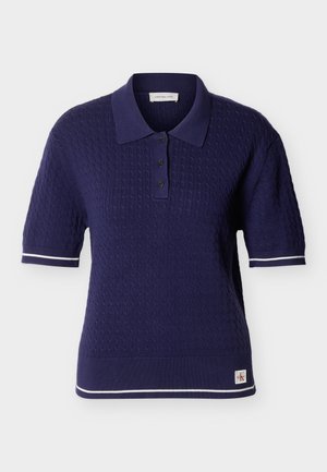 Πλεκτό polo μπλούζα σε σκούρο μπλε χρώμα με κοντά μανίκια και σχέδιο καλωδίων, με τριάκτινο κούμπωμα, λευκή ρίγα στις μανσέτες και στο τελείωμα, και μικρό λογότυπο Calvin Klein.