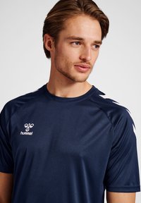 T-shirt de sport à manches courtes navy avec le logo Hummel, présentant des accents blancs sur les épaules et un design en tissu lisse qui évacue l'humidité.