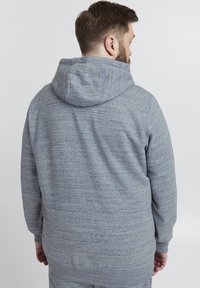 Grå hettegenser med en teksturert, heathered finish. Har en stor hette og lange ermer med ribbestrikkede mansjetter, designet for komfort og varme.