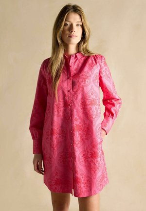 Pink shirt dress featuring a button-down front, long sleeves, and a paisley pattern. Made of smooth fabric with side pockets.