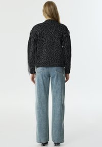 Cárdigan negro de punto con patrón texturizado, mangas texturizadas y detalles con flecos. Combinado con jeans de pierna ancha de color azul claro.