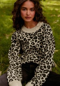 Pulover s uzorkom leoparda od pletenine, s rebrastim okruglim izrezom i dugim rukavima, s laganom krem bazom i tamnim mrljama, u kombinaciji s tamnim trapericama.