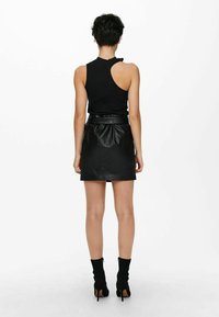 Débardeur noir côtelé avec un dos asymétrique, associé à une mini-jupe en cuir noir taille haute et des bottines noires.