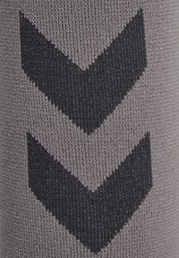 Grauer Stoff mit gerippter Textur, der zwei große schwarze Chevron-Muster zeigt. Das Design erzeugt einen geschichteten visuellen Effekt.