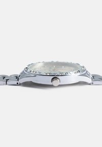 Silver metal watch with a textured bezel, crystal accents, a round face, and a polished link bracelet. Features a side crown for adjustments.