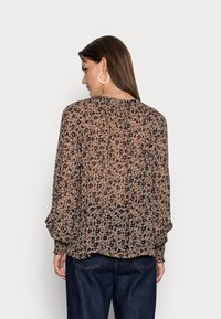 Blusa de estampado floral em bege e azul marinho, mangas longas com punhos franzidos, tecido leve e transparente, decote redondo, design fluido.