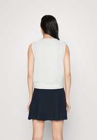 Top senza maniche grigio chiaro con scollo rotondo, abbinato a una gonna plissettata blu scuro. Tessuto liscio, design minimalista e stile aderente.