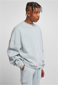 Felpa oversize azzurra, con collo a giro ribbed, maniche lunghe e una texture morbida, abbinata a pantaloni azzurri coordinati.