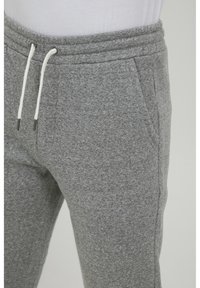 Gray sweatpants made of soft fabric, featuring an elastic waistband with a white drawstring, side pockets, and a tapered leg design.