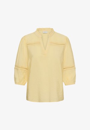 Svetložltá blúzka s volánovým golierom, výstrihom do V, tromi štvrtinovými nafúknutými rukávmi a čipkovými ozdobami na hrudi a rukávoch.