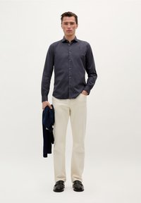 Cămașă bleu închis cu mânecă lungă, butonat�ă, cu guler; pantaloni bej; ținând un pulover bleu închis; pantofi negri; design simplu pe un fundal deschis.