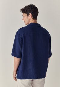  mornarsko plava kratka majica s teksturiranim tkanjem, ovratnikom i ležernim krojem, s ravnim rubom i kutijastim siluetom.