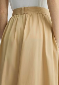 Gonna beige con vita arricciata, tessuto strutturato e una tasca laterale. La vita è piatta e presenta un dettaglio con passante per cintura.