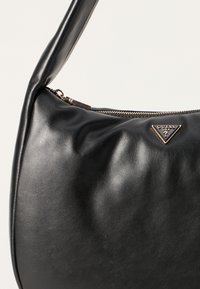 Bolsa de ombro em couro preto com uma textura suave, apresentando um fecho de zip e um detalhe em logótipo triangular dourado na frente.