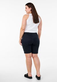 Pantalones cortos de denim negro con una cintura ajustada, diseño de pierna recta y bolsillos traseros. Combinados con una blusa blanca sin mangas y calzado negro.