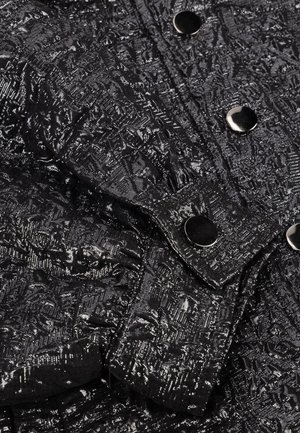 Zwart textiel met een metallic glans, voorzien van drukknopen op een opgevouwen manchet en aangrenzende gebieden.