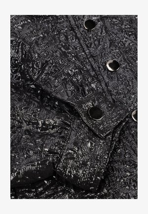 Zwart textiel met een metallic glans, voorzien van drukknopen op een opgevouwen manchet en aangrenzende gebieden.