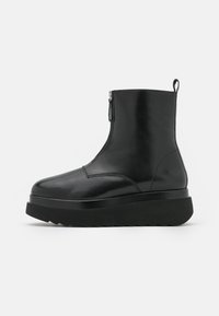 Černá kožená kotníková bota s hladkým povrchem, kulatou špičkou, bočním zipem a silnou černou platformou. Minimalistický design a bezproblémová konstrukce.