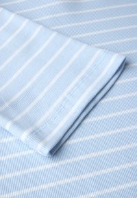 Ljusblått ribbtyg med tunna vita ränder. Nära bild av en vikt ärm som visar sömnadsdetaljer och textur.