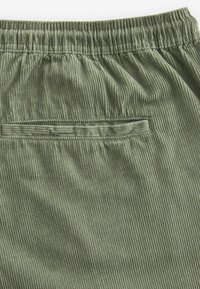 Groene corduroy broek met een elastische tailleband, voorzien van een achterzak en verticale ribbeltextuur. Zachte stof met een subtiele glans.