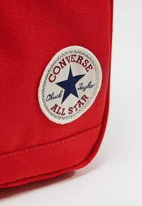 Červená látková část tašky Converse All Star zobrazující bílou kulatou nášivku s modrou hvězdou a červeným textem.