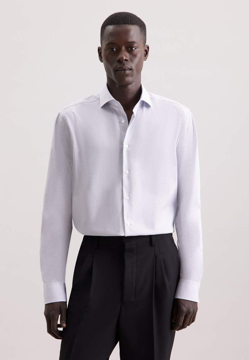 Camicia bianca a maniche lunghe con un sottile motivo testurizzato, colletto all'inglese e polsini singoli, abbinata a pantaloni neri sartoriali.