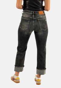 Jeans in denim nero con finitura distressed, con risvolti, due tasche posteriori e una patch in pelle con il marchio in vita.