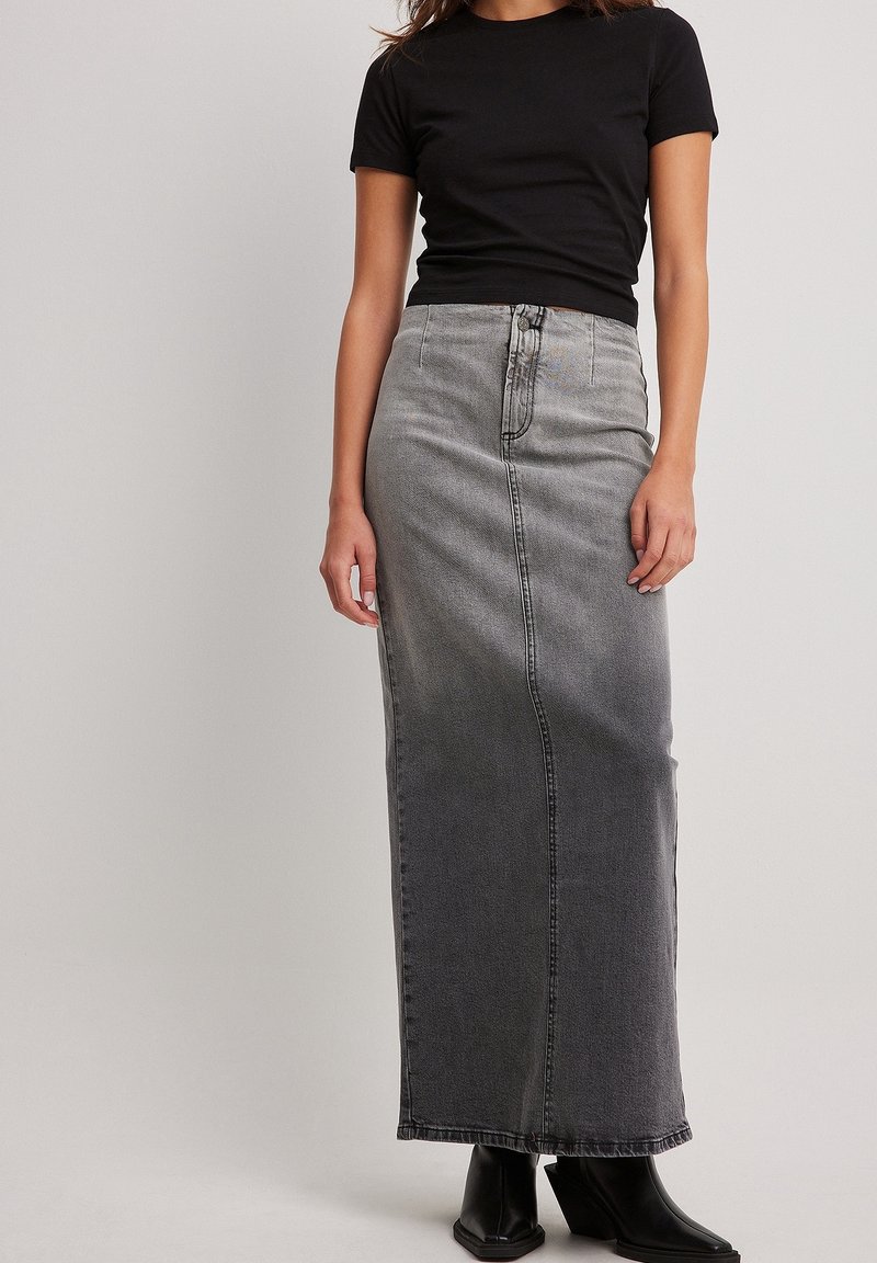 Camiseta negra combinada con una falda de mezclilla gris de tiro alto y longitud hasta el tobillo, con un acabado desgastado y detalles de costuras visibles.