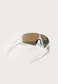 Baltas sporta saulesbrilles ar lielu, izliekta brūna un zaļa stikla lēcu. Iespējams, eleganti, tievie rāmi un melni gumijas akcenti uz deguna spilventiņiem.