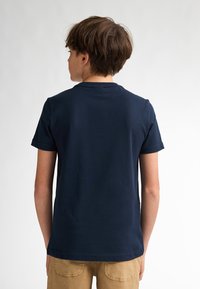 Tricou din bumbac bleu marin cu mâneci scurte, guler rotund și croială relaxată, văzut din spate, având o textură netedă.