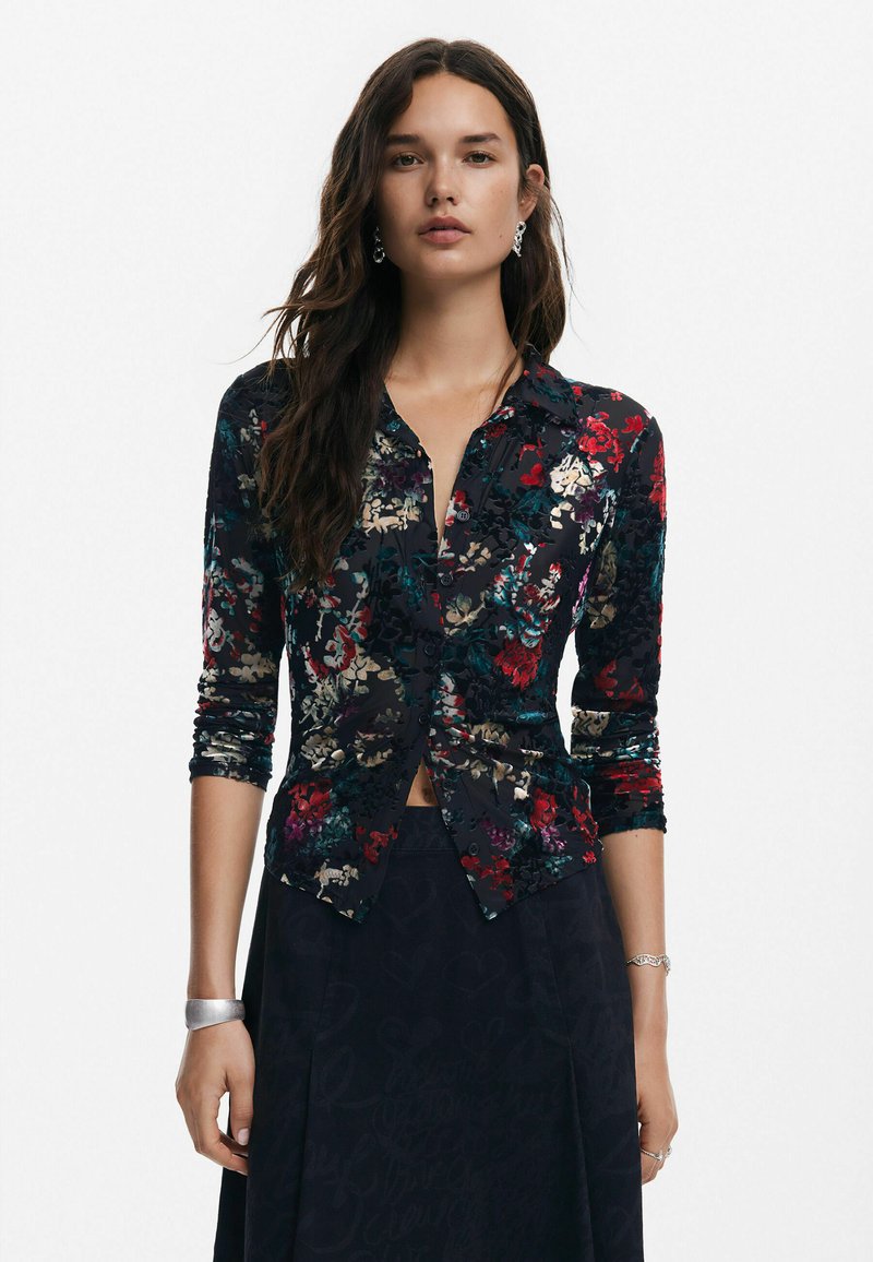 Tumedas kangas lilleline nööbiga särk, millel on punased, rohelised ja kuldsed mustrid. Pikeed varrukad ja istuv lõige, millel on peened tekstuurilised detailid.