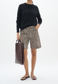 Suéter negro de punto, pantalones cortos beige con estampado de leopardo, bolso marrón y chanclas negras. Conjunto casual con un corte relajado y patrones.