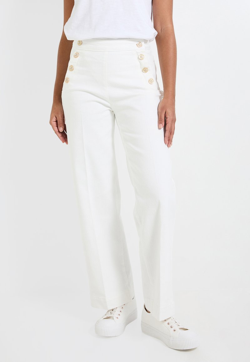 Pantalones blancos de cintura alta con perneras anchas, que presentan seis botones decorativos dorados en el lateral y una tela suave y texturizada. Combinados con zapatillas blancas.