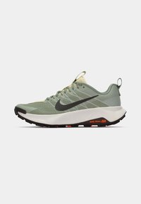 Shoe de trail da Nike em verde claro com um cabedal texturizado, sola preta e detalhes em laranja, apresentando um bico arredondado e fecho de atacadores.