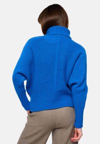 Pull en tricot bleu royal avec un col haut, un jeu de textures en côtes et une coupe décontractée. Doté d'une couture arrière fendue et de manches surdimensionnées.