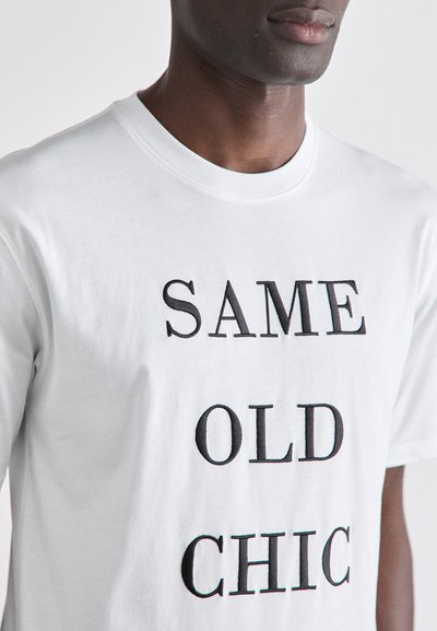 White cotton t-shirt featuring black embroidered text "SAME OLD CHIC." Classic crew neck design with short sleeves, soft texture.