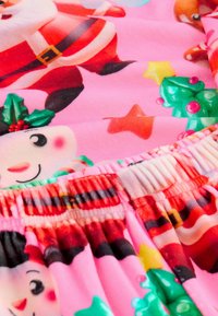 Fleece-tyg med färgglada julmotiv, inklusive jultomte, kristyr och julprydnader, med en rosa bakgrund och elastisk midja.